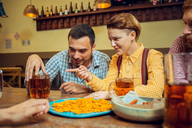 The people, leisure, friendship and communication concept - happy friends drinking beer, talking and clinking glasses at bar or pub