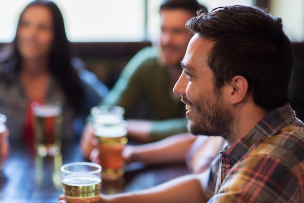 people, leisure, friendship and communication concept - happy man with friends drinking beer at bar or pub