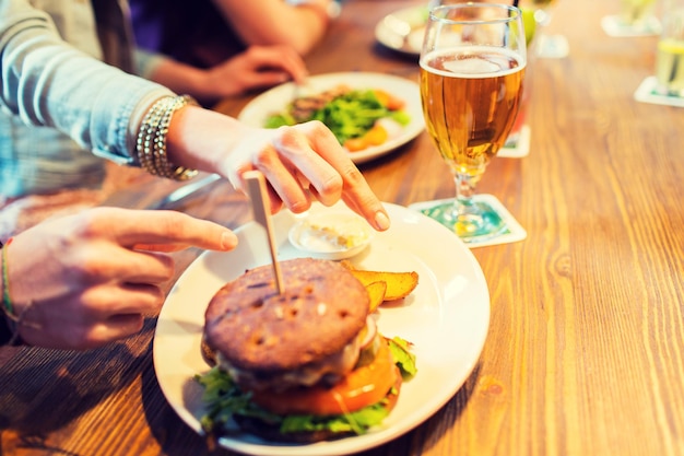 people, leisure, friendship, eating and food concept - close up of friends hands with burger at bar or pub