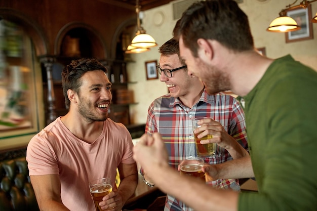 people, leisure, friendship and entertainment concept - happy football fans or male friends drinking beer and celebrating victory at bar or pub