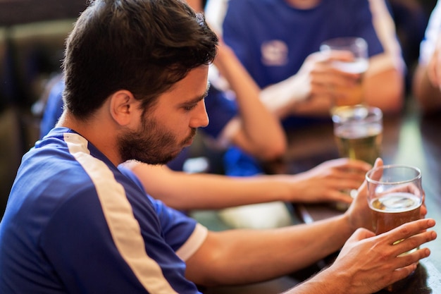 people, leisure, soccer and sport concept - unhappy football fans or friends with beer at bar or pub