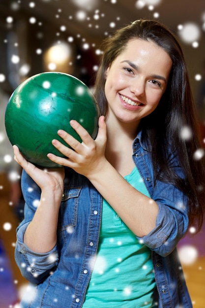 people, leisure, sport and entertainment concept - happy young woman holding ball in bowling club at winter season