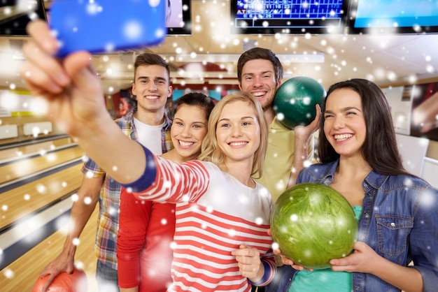 people, leisure, sport, friendship and entertainment concept - happy friends taking selfie with smartphone in bowling club at winter season