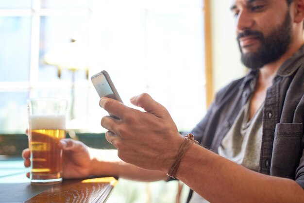 people, leisure and technology concept - close up of man with smartphone drinking beer and reading message at bar or pub