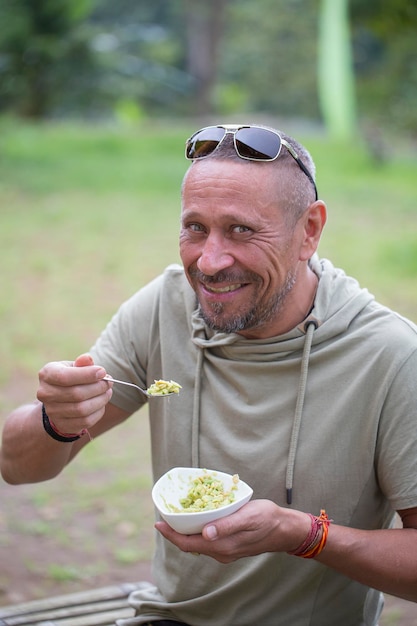 People and lifestyle concept Happy middleaged man eating a avocado guacamole in nature closeup portrait