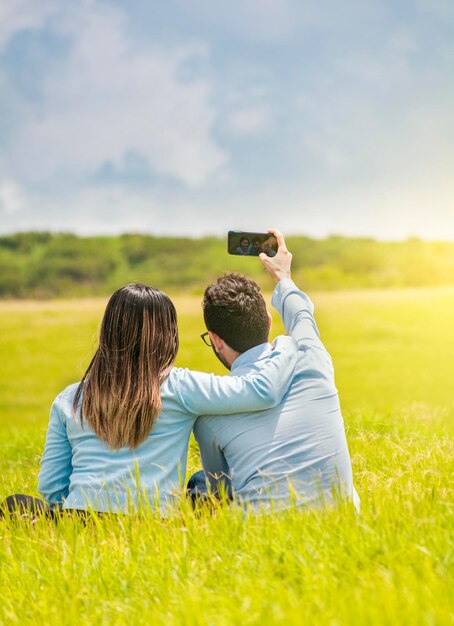 People in love taking selfies in the field with their smartphone Smiling couple in love sitting on the grass taking selfies Young couple in love taking a selfie in the field