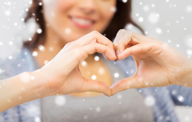 people, love, valentines day, christmas and  charity concept - close up of happy young woman showing heart with hands over snow