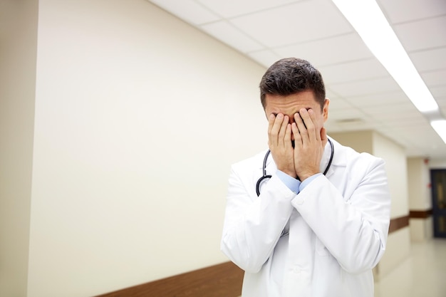 people, medicine, healthcare and sorrow concept - sad or crying male doctor at hospital corridor