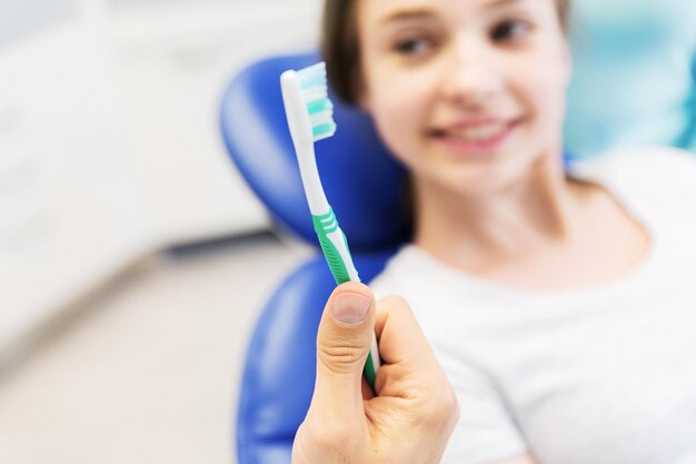 people, medicine, stomatology and health care concept -close up of dentist hand holding toothbrush and patient girl at dental clinic office