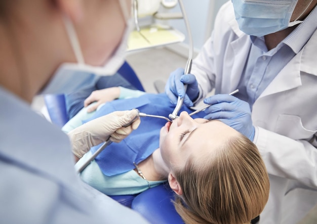 people, medicine, stomatology and health care concept - close up of dentists and assistant with mirror, drill and dental air water gun spray treating female patient teeth at dental clinic