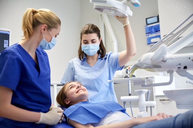 people, medicine, stomatology and health care concept - happy female dentist with assistant and patient girl at dental clinic office