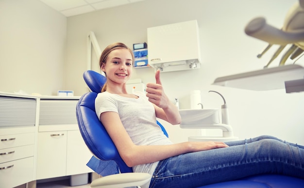 people, medicine, stomatology and health care concept - happy patient girl showing thumbs up at dental clinic office