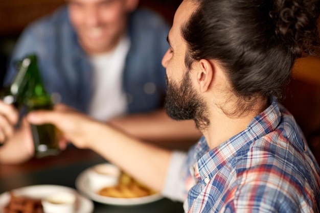 people, men, leisure, friendship and celebration concept - happy male friends drinking beer and clinking bottles at bar or pub