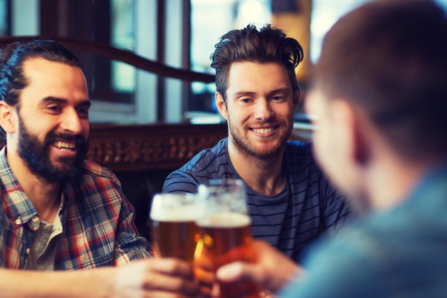 people, men, leisure, friendship and celebration concept - happy male friends drinking beer and clinking glasses at bar or pub