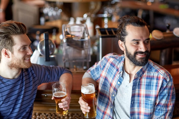 people, men, leisure, friendship and party concept - happy male friends drinking draft beer at bar or pub