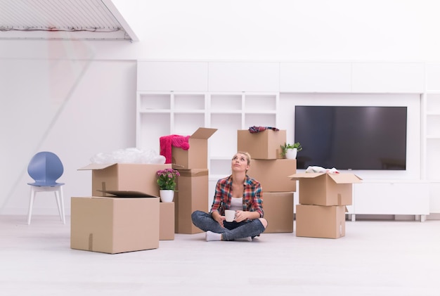 people, moving new place and repair concept   happy beautiful  young woman with many cardboard boxes sitting on floor with Cup at home