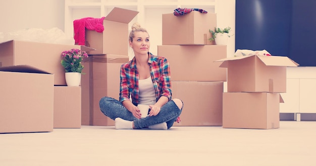 Photo people, moving new place and repair concept   happy beautiful  young woman with many cardboard boxes sitting on floor with cup at home