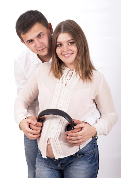 People and music Pregnant woman and man in white shirts and jeans with headphones on white background