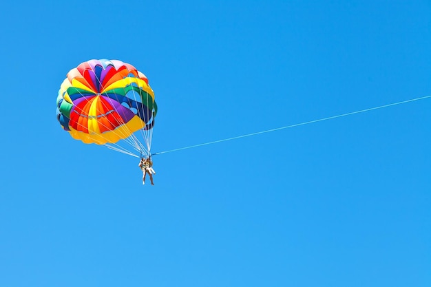 People parascending on parachute in blue sky