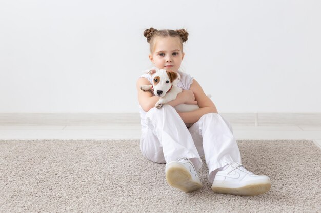 People pets and animal concept little girl sitting on the floor over white wall and holding