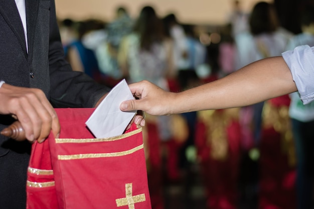 Photo people putting tithing into velvet offering bag in church