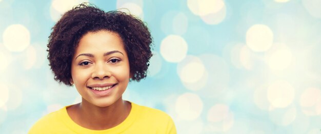 people, race, ethnicity and portrait concept - happy african american young woman face over blue lights background