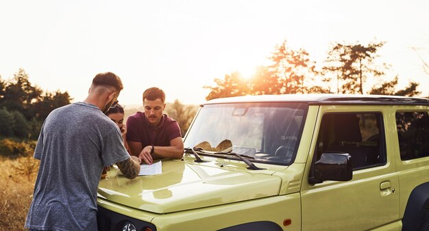 People reading map that lying on the hood of the automobile