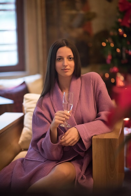 people, and relaxation concept   beautiful young woman in bath robe drinking champagne at spa over holidays lights background