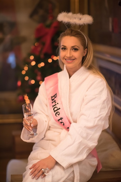 people, and relaxation concept   beautiful young woman in bath robe drinking champagne at spa over holidays lights background