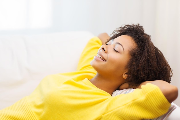 people, rest, comfort and leisure concept - happy african young woman relaxing or dreaming at home