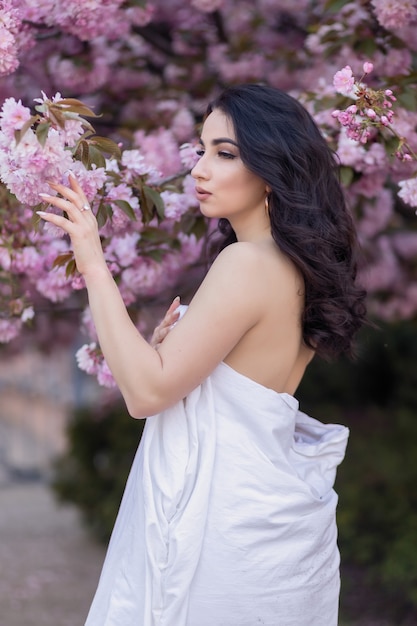 People, rest, comfort and leisure concept - Young woman through the evening streets wrapped in a blanket. Beautiful young girl in the park and a flowering tree sakura