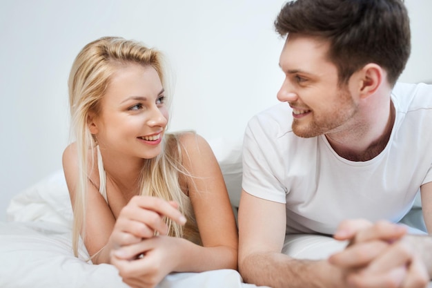 people, rest, love, relationships and happiness concept - happy couple lying in bed at home