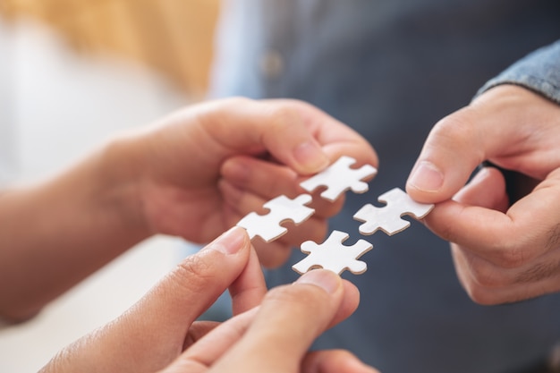 people's hands holding and putting a piece of white jigsaw puzzle together