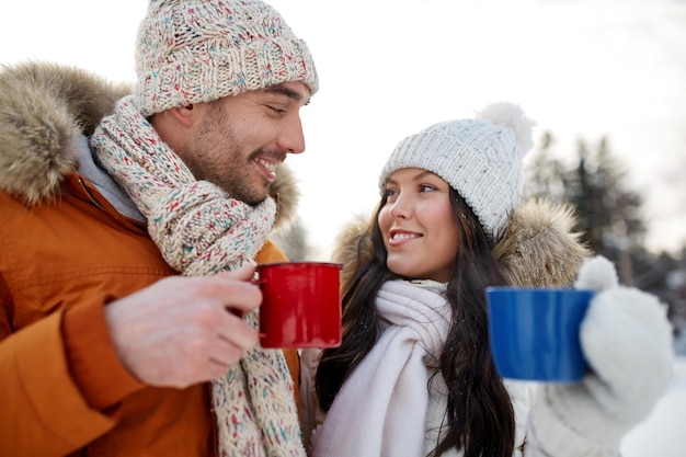 people, season, love, drinks and leisure concept - happy couple holding hot tea cups over winter landscape