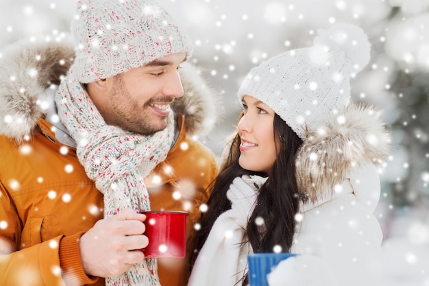 people, season, love, drinks and leisure concept - happy couple holding hot tea cups over winter landscape