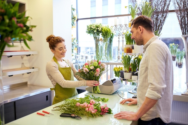 people, shopping, sale, floristry and consumerism concept - happy smiling florist woman making bouquet for and man or customer at flower shop