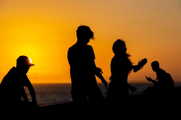 Photo people in silhouette are seen enjoying the sunset on rio vermelho beach in the city of salvador bahia