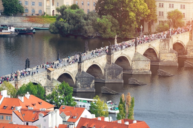 People on a stone bridge across the river with a tower and sculptures in a beautiful old city Toned