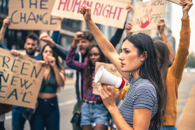 People strike against climate change and pollution, portrait of young woman holding a megaphone and raise arm, green new deal protest, warm filter