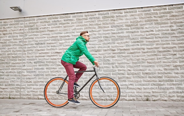 people, style, leisure and lifestyle - young hipster man riding fixed gear bike on city street over brick wall background