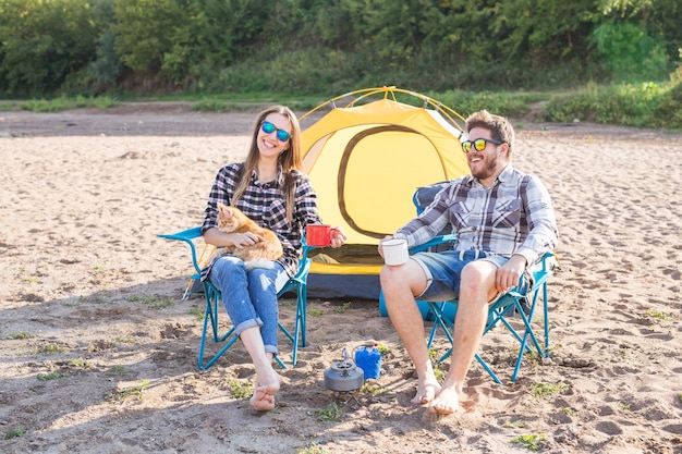 People, summer tourism and nature concept - young couple drinking tea near tent.