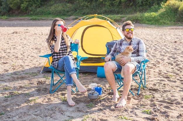 people, summer tourism and nature concept - young couple drinking tea near tent