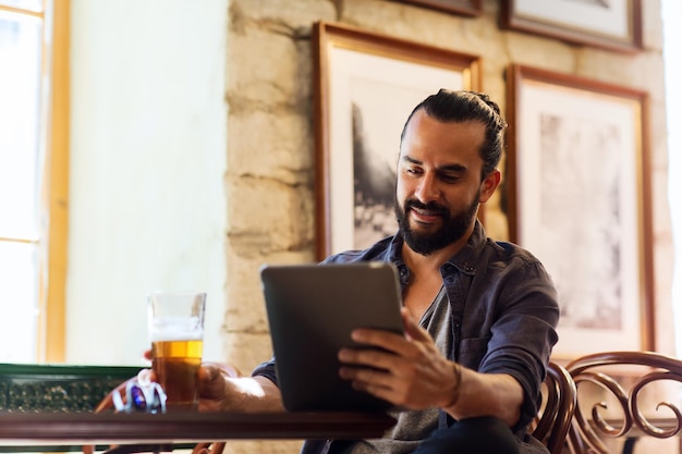 people and technology concept - happy man with tablet pc computer drinking beer at bar or pub