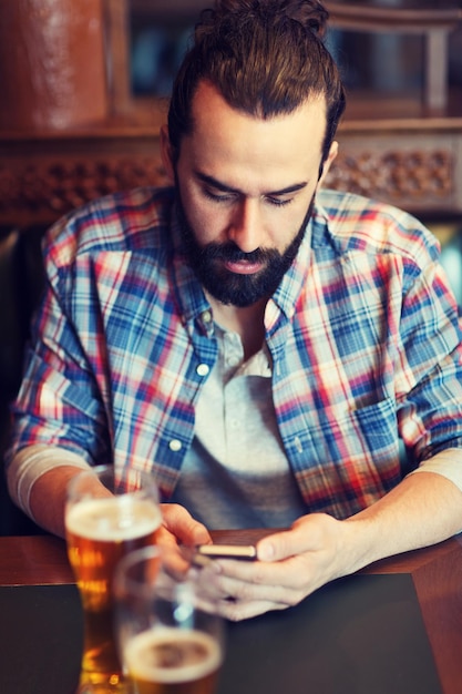 people and technology concept - man with smartphone drinking beer and reading message at bar