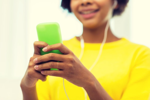 people, technology and leisure concept - close up of happy african american young woman sitting on sofa with smartphone and headphones listening to music at home