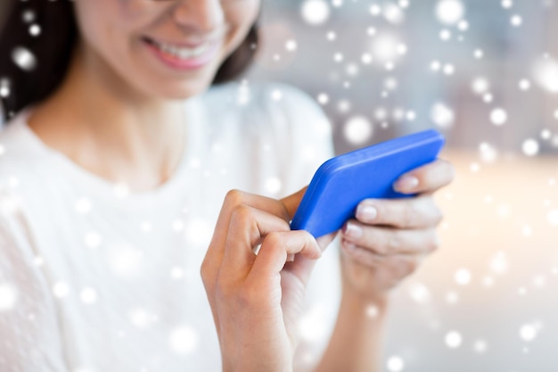 people, technology and lifestyle concept - close up of woman with smartphone at cafe over snow effect