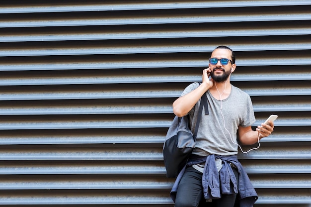 people, technology, travel and tourism - man with earphones, smartphone and bag on city street and listening to music