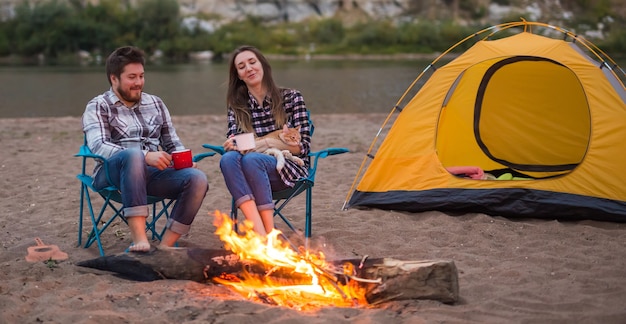 People, tourism and nature concept - Man embrace woman sitting near a fire.