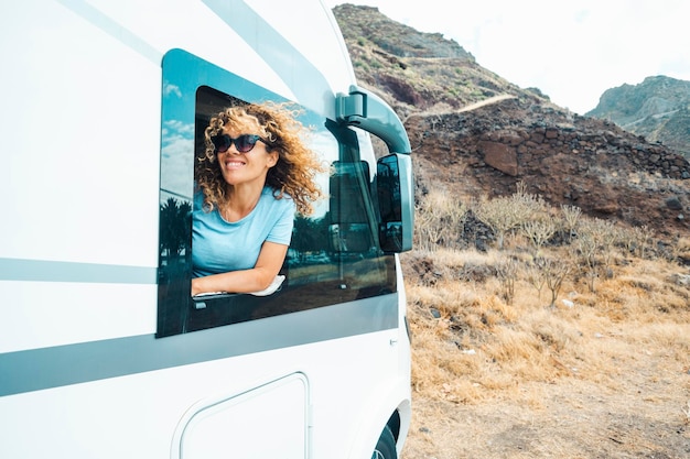 People and travel holiday vacation destination Happy young adult woman smile and enjoy nature off road parking outside the window of her modern motor home camper van Female traveler