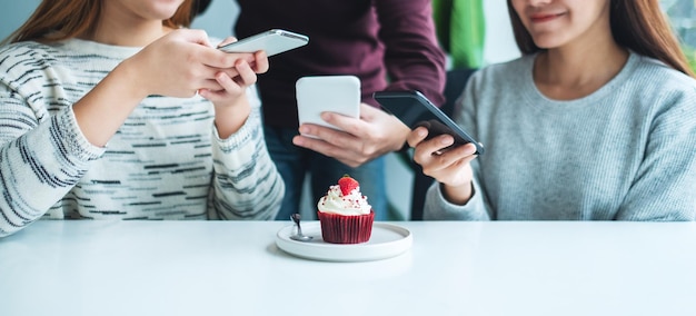 People using mobile phone to take a photo of a cupcake before eat in cafe